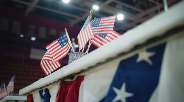 Elections in the United States of America. Close up of table for voting registration with American flags standing at polling place. Presidential race and election coverage. Civic duty and patriotism.