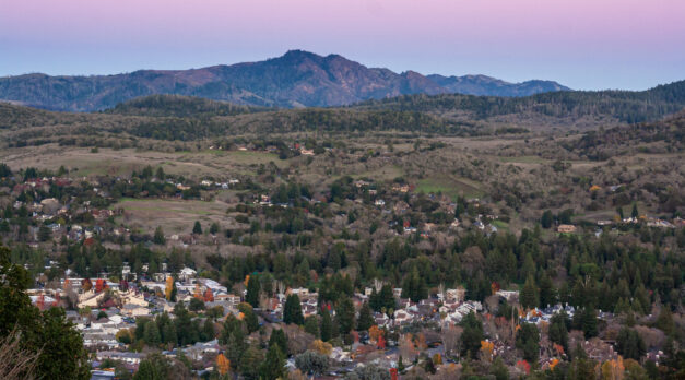 Aerial view of the town of Santa Rosa, California, nestled in a valley at sunset beneath a mountain. Rural community in Sonoma County wine country at dusk.