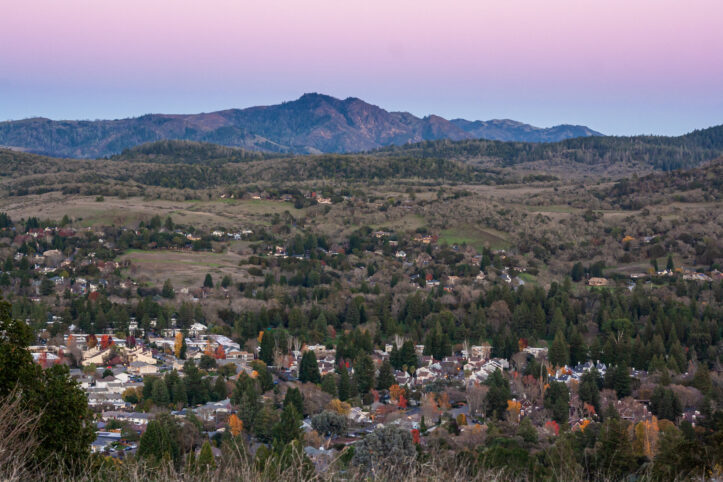 Aerial view of the town of Santa Rosa, California, nestled in a valley at sunset beneath a mountain. Rural community in Sonoma County wine country at dusk.