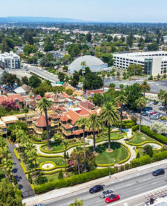 Aerial view of historic Winchester Mystery House with its lush gardens, surrounded by modern office and residential buildings and a busy street - San Jose, California, USA - July 14, 2024